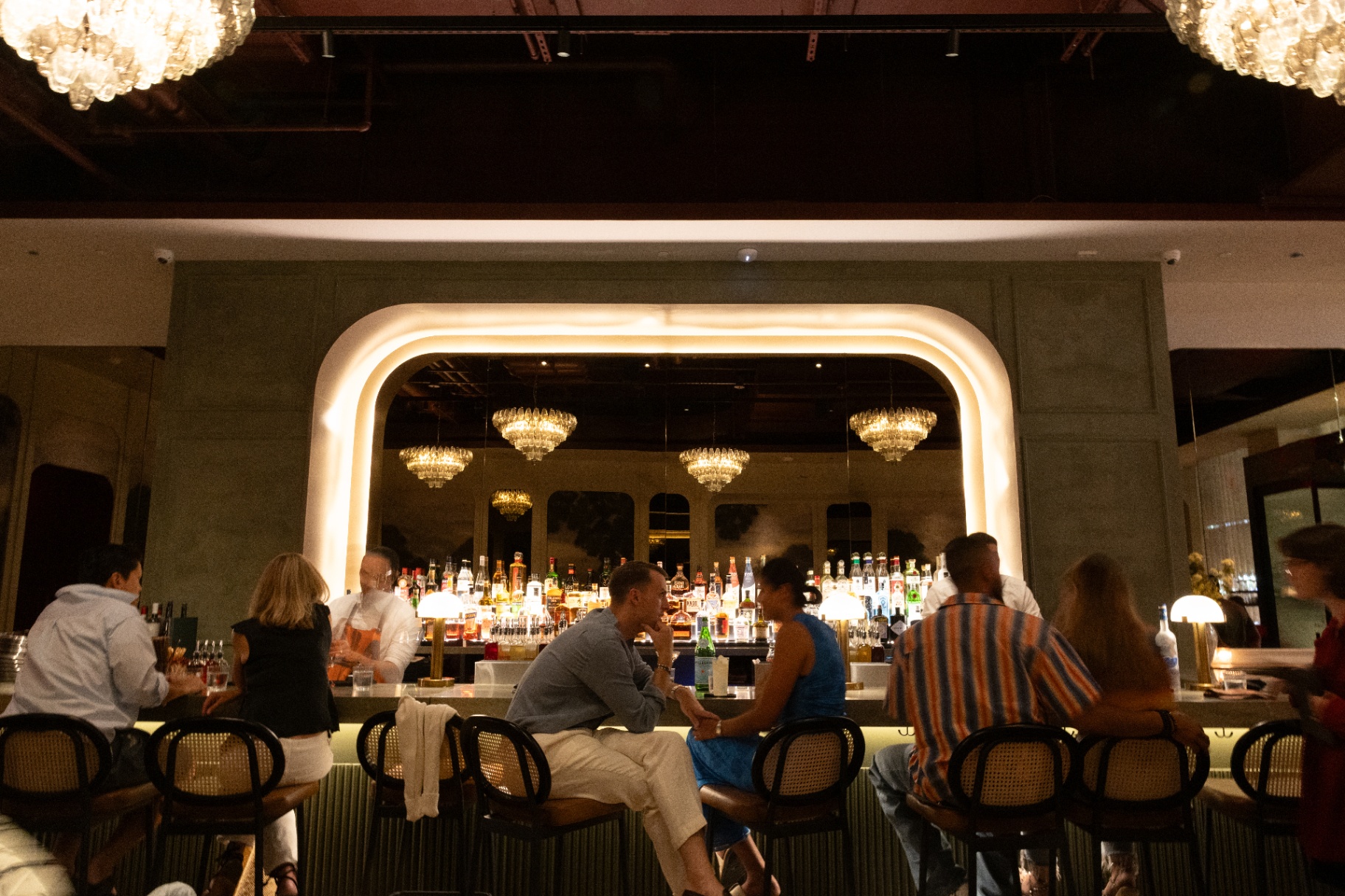 Atmospheric hospitality bar interior with chandeliers and guests gathered at the counter